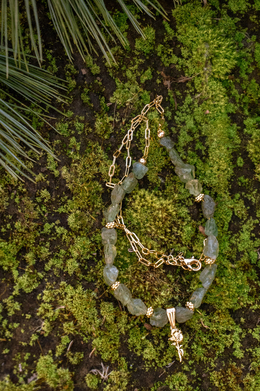 Gold chain and beaded bracelet on a textured green surface